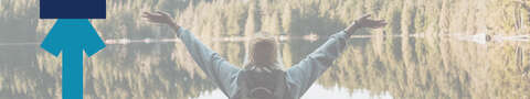 A woman raises her arms joyfully as she stands in front of a beautiful landscape.