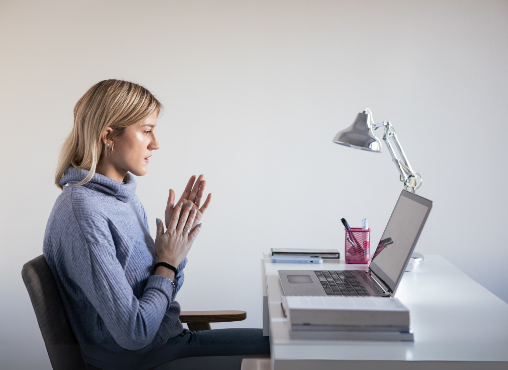 A woman sitting at a desk, speaking animatedly into a laptop.