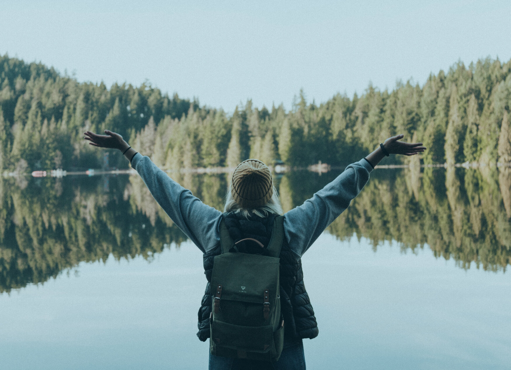 A woman raises her arms joyfully as she stands in front of a beautiful landscape.